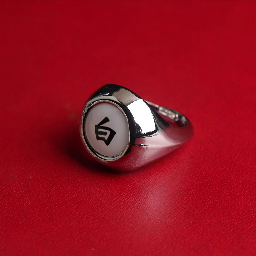 Bague en métal argenté avec un symbole blanc et noir sur un fond rouge. La bague est une réplique des anneaux de l'univers Naruto.