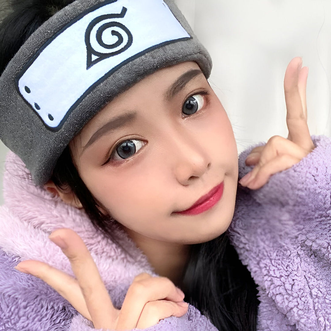 Une jeune femme portant un bandeau gris avec le symbole de Konohagakure, le village caché de la feuille, de l'anime Naruto. Elle porte également un pull violet et sourit à la caméra.