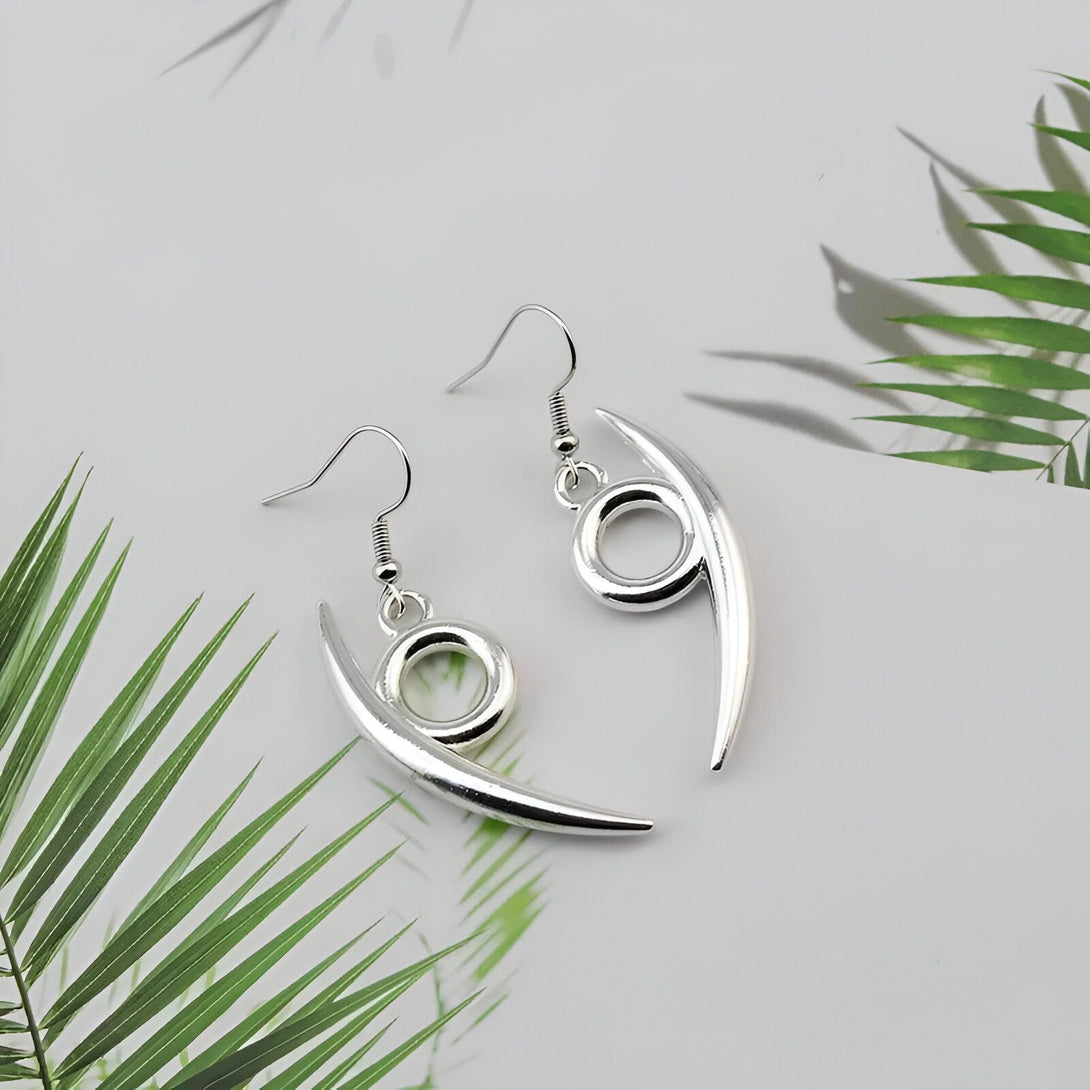 Une paire de boucles d'oreilles argentées en forme de croissant de lune avec un cercle au centre, inspiré de l'univers de Naruto.