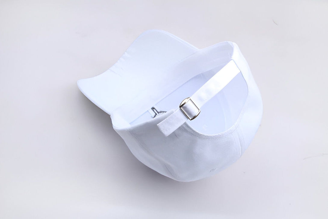 Casquette blanche en coton avec une fermeture à boucle en métal. La casquette est sur un fond blanc.