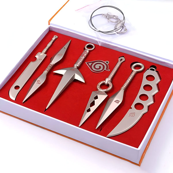Ensemble de 6 armes en métal de Naruto, comprenant un kunai, des shurikens, un couteau, un pendentif et un porte-clés. L'ensemble est présenté dans une boîte rouge.