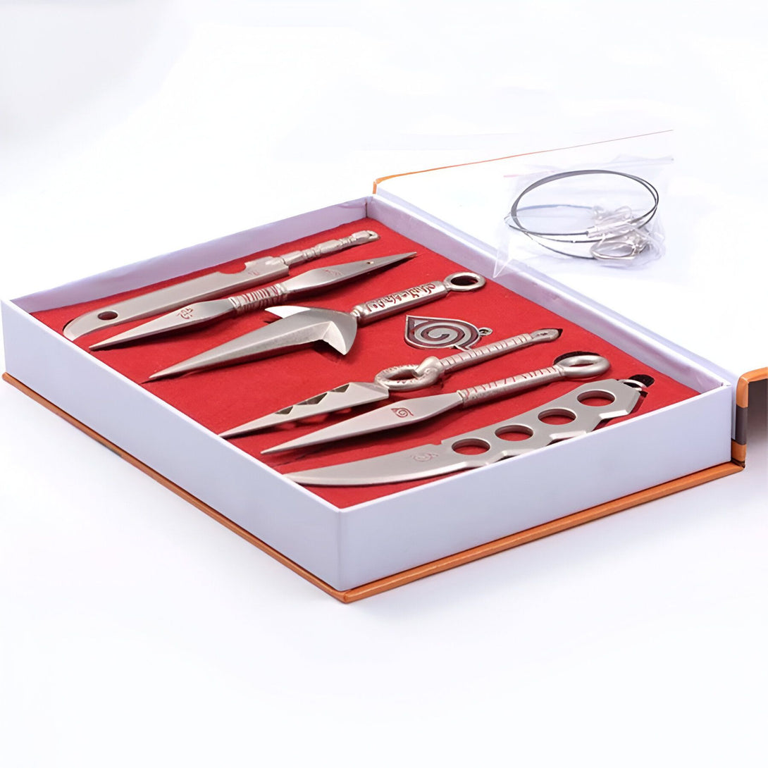 Ensemble de 6 armes de jet Naruto en métal, comprenant des kunais, des shurikens et un symbole du clan Uchiwa, présenté dans un coffret cadeau.