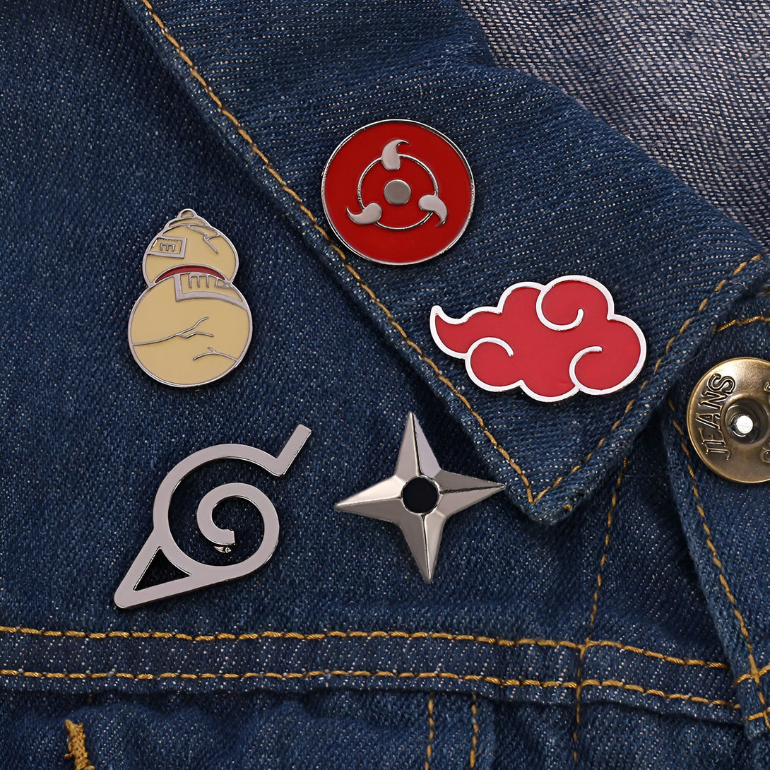 Cinq épingles de l'anime Naruto sur une veste en jean bleue. Les épingles représentent le symbole du village caché de la feuille, le nuage rouge, le symbole de l'Akatsuki, un gourde et un shuriken.