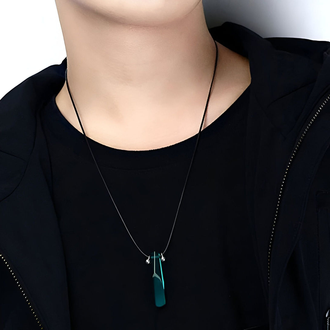 Un collier avec un pendentif vert en forme de lame, porté par un homme portant un t-shirt noir.