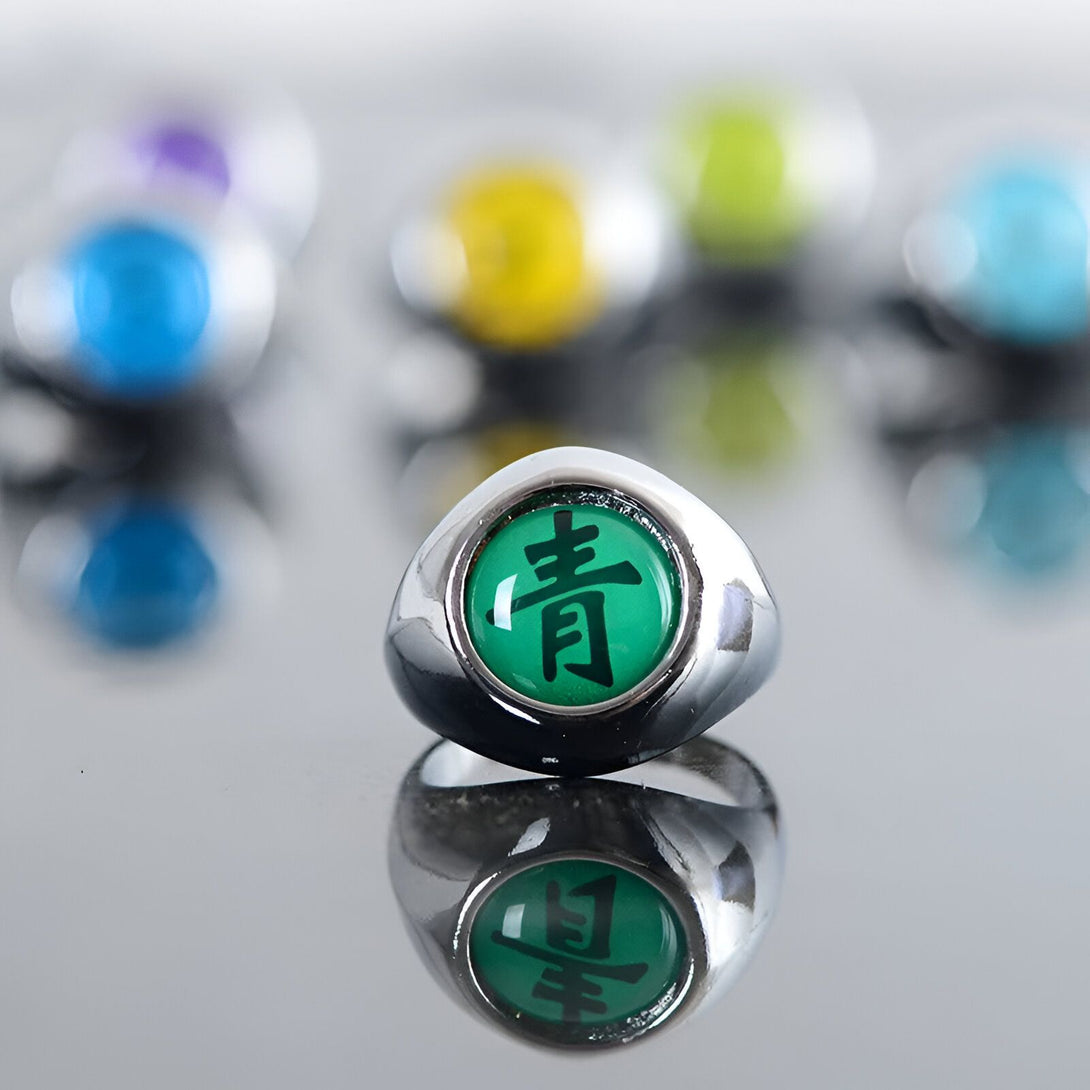 Bague en argent avec un symbole vert représentant le clan Uchiwa de l'univers Naruto.  La bague est posée sur une surface réfléchissante.