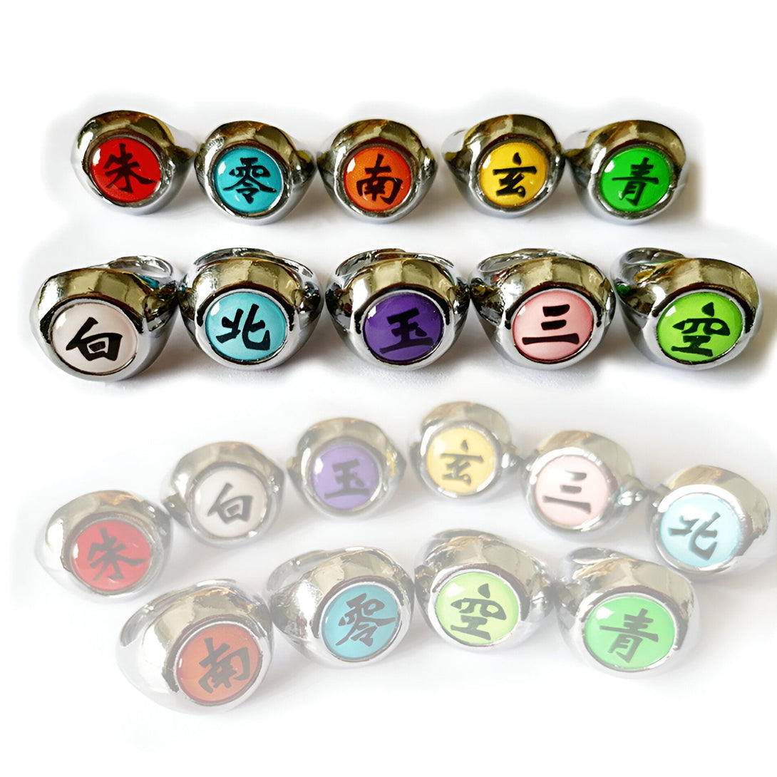 Ensemble de 12 bagues Naruto en métal avec des symboles différents. Les bagues sont de couleur argentée et les symboles sont noirs sur des fonds colorés. Il y a 12 bagues en total.