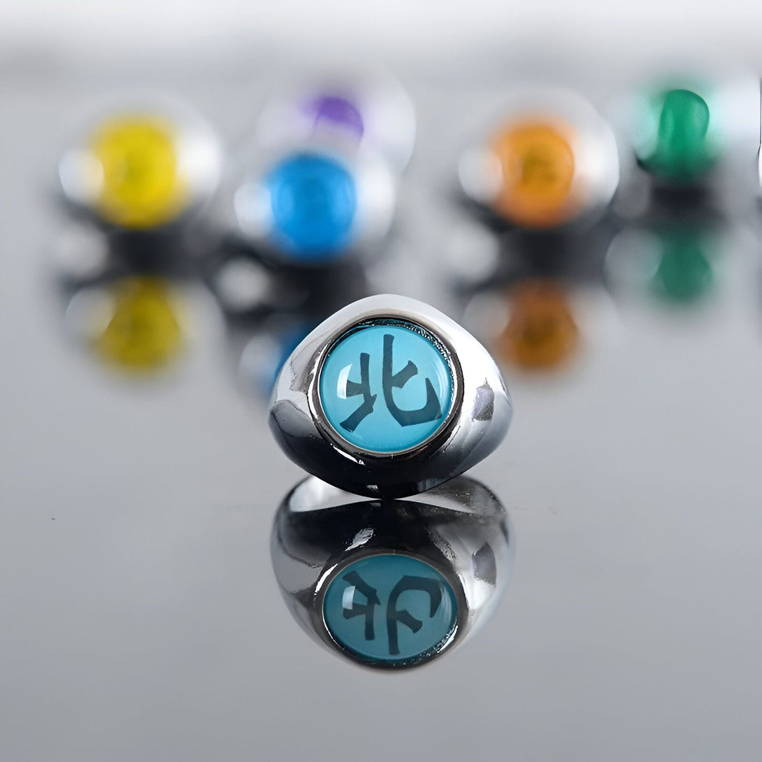 Bague de Sharingan bleu clair avec le symbole "Byakugan" en kanji blanc, issue de l'univers de Naruto. La bague est en métal argenté et est reflétée sur une surface brillante.
