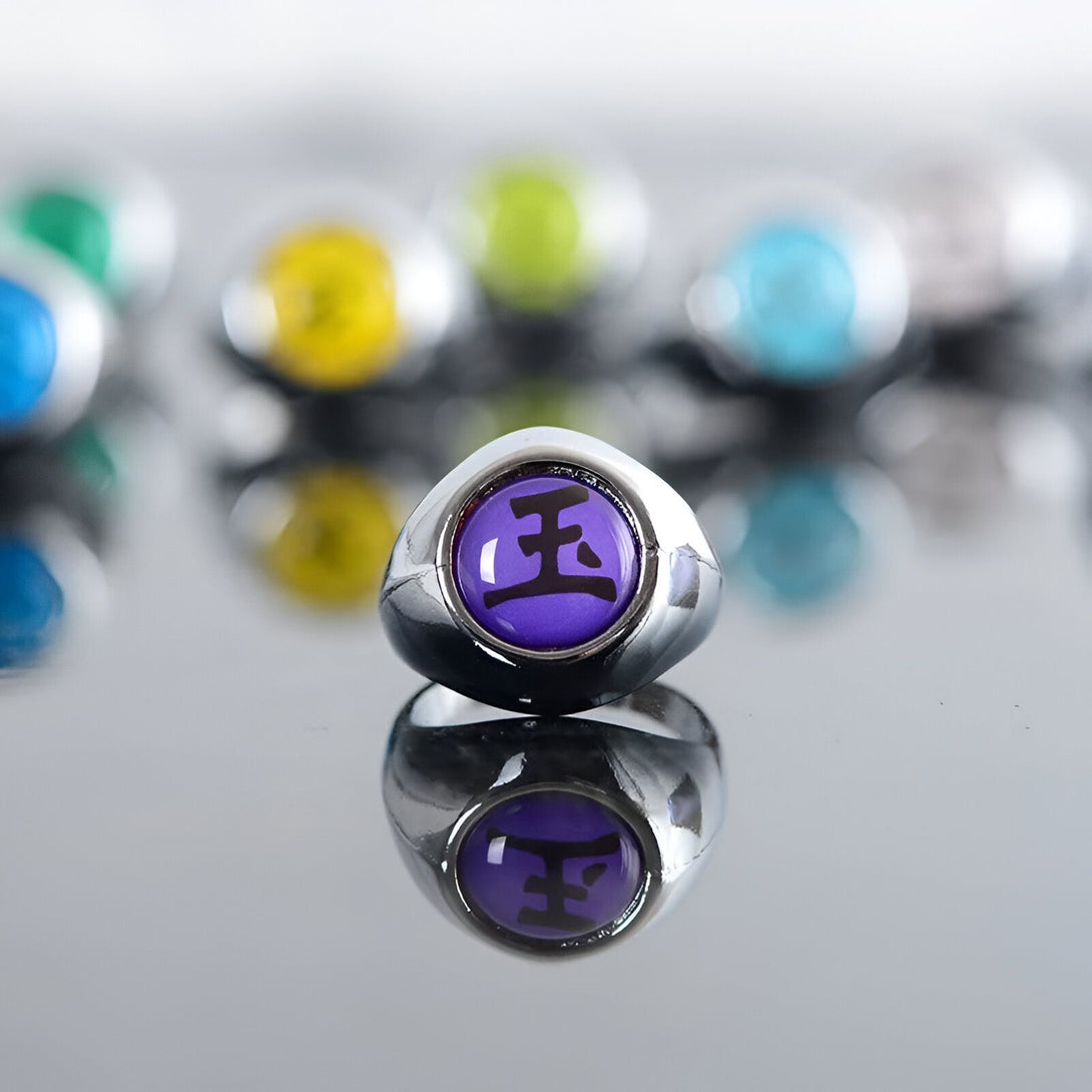 Bague en métal argenté avec un symbole violet de l'univers Naruto, représentant le Rinnegan. La bague est réfléchie sur une surface brillante.