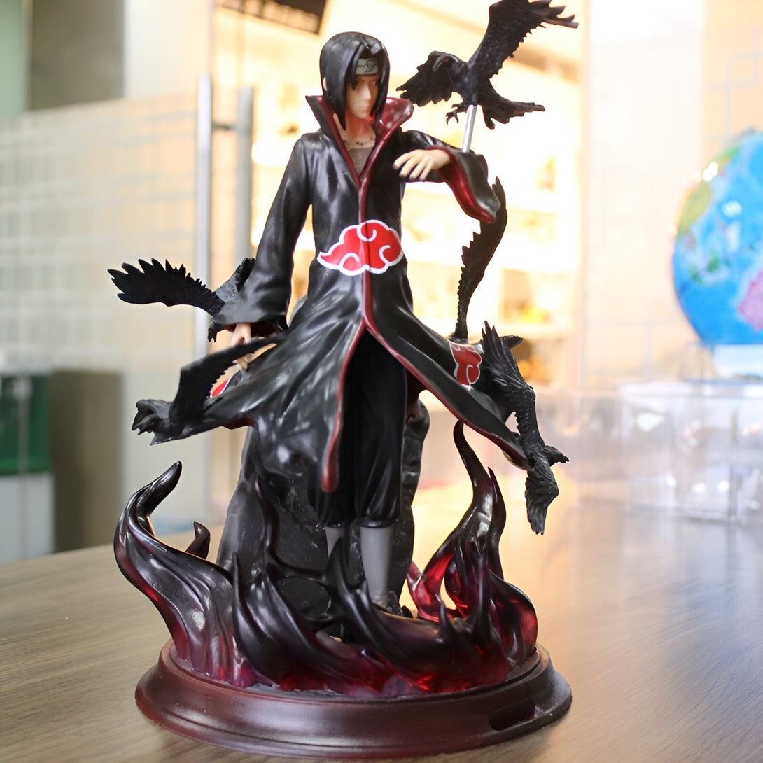 Figur de collection de Itachi Uchiha de Naruto, vêtu de son manteau rouge et noir emblématique, entouré de corbeaux noirs et de flammes. La figurine est posée sur un socle noir et rouge.