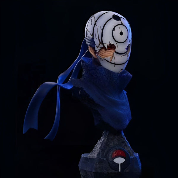 Buste de personnage de l'anime Naruto, portant un masque blanc avec un motif circulaire et une bande bleue autour du cou. Le buste est placé sur un socle noir avec le symbole du village de Konoha.