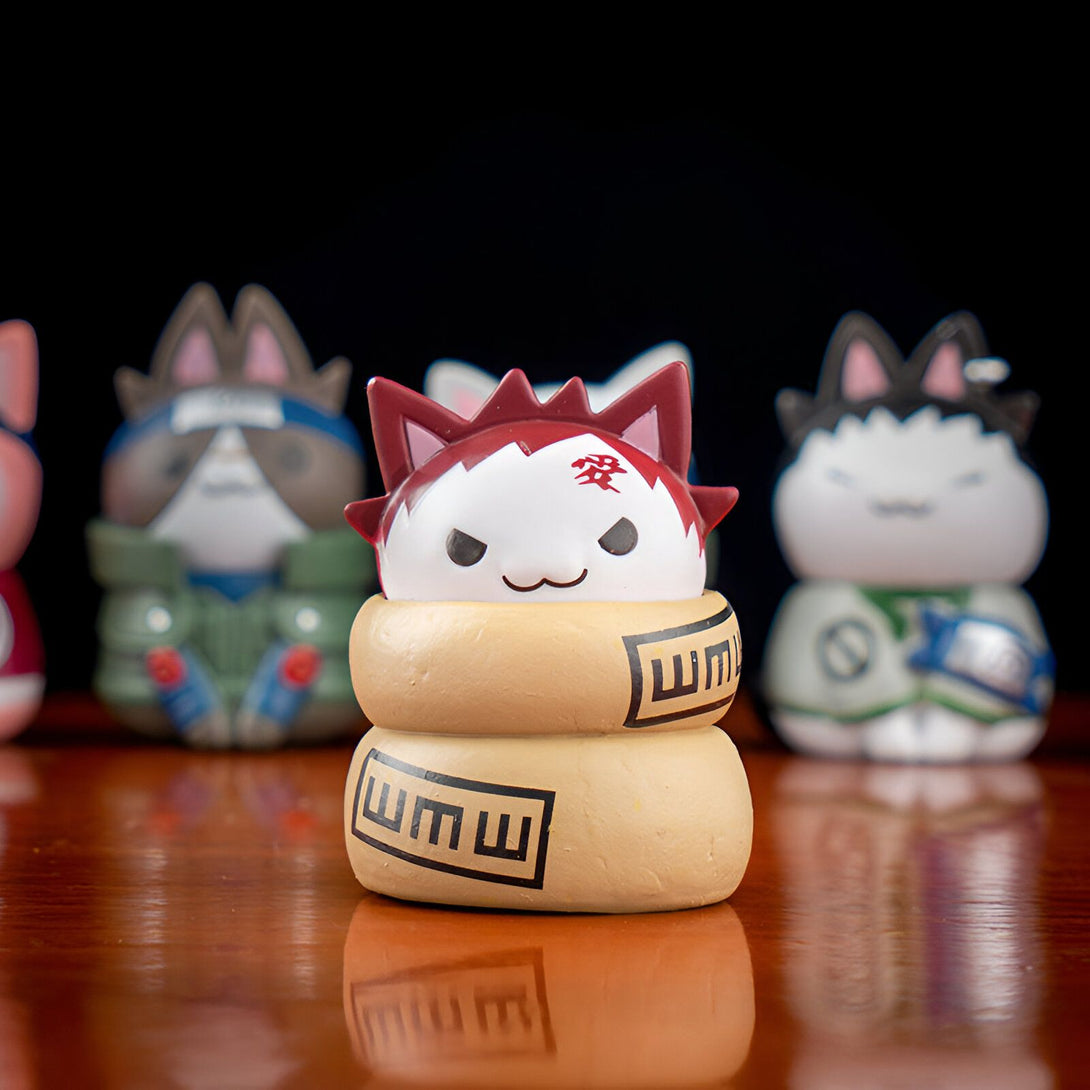 Une figurine de chat Naruto enroulé dans une écharpe de feuille, avec le symbole du clan Uzumaki. La figurine est peinte avec des couleurs vives et a un design adorable.