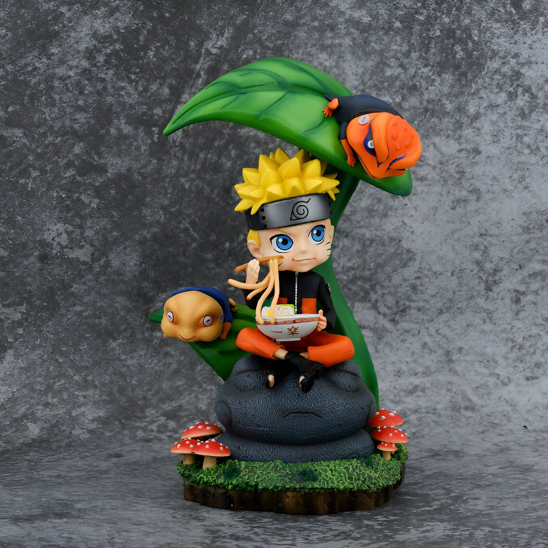 Naruto Uzumaki en figurine chibi, assis sur une roche avec son crapaud Gamakichi et son crapaud géant Gamabunta. Il est en train de manger des nouilles dans un bol.