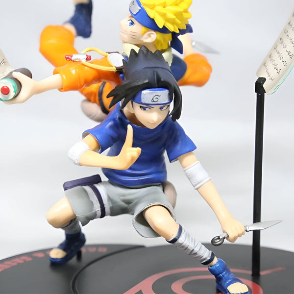 Figure de collection Naruto et Sasuke de l'anime Naruto. Les deux personnages sont représentés dans une posture dynamique, Sasuke tenant un kunai dans sa main droite. La figurine est posée sur un socle avec le symbole du village caché de Konoha.