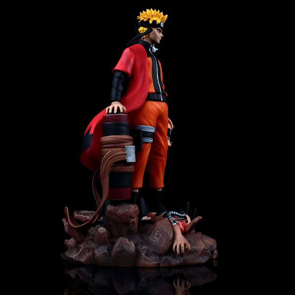 Naruto Uzumaki, le personnage principal de l'anime Naruto, représenté dans une figurine de collection. Il est debout sur un socle rocheux avec son emblématique veste rouge et son bandeau. On peut également voir un autre personnage couché au sol.