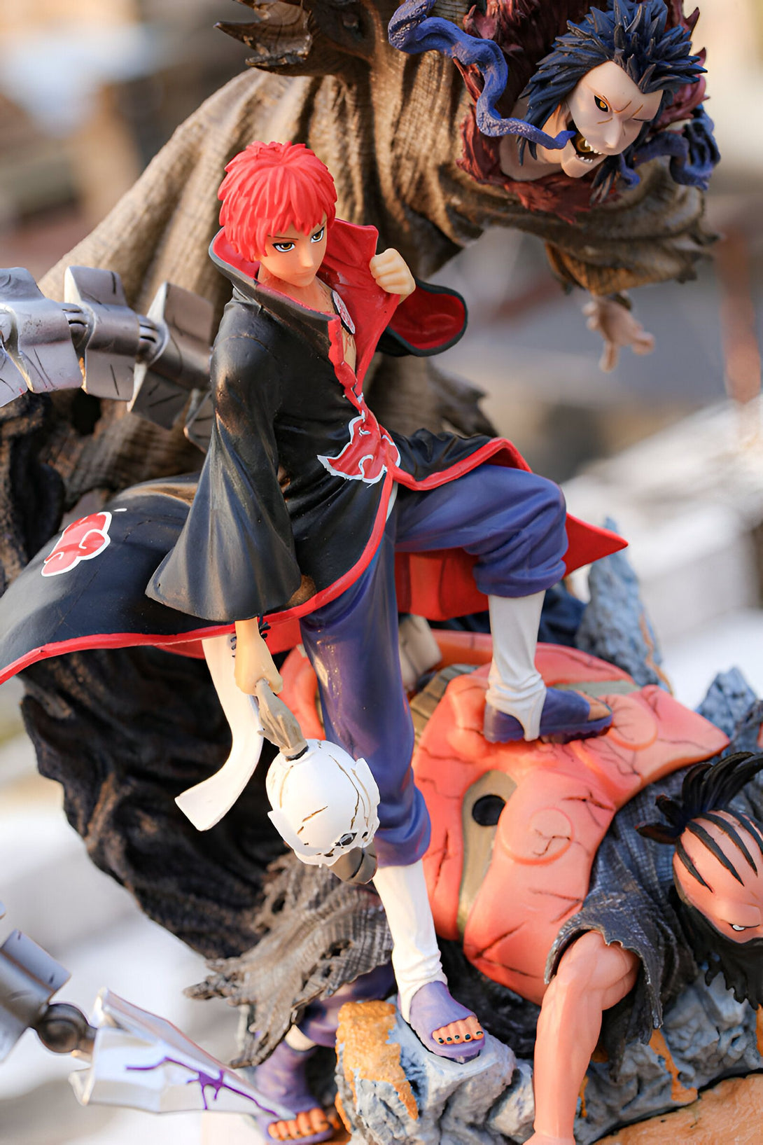 Figurines Naruto : Un personnage de Naruto se tient debout sur une base avec un autre personnage. Le personnage principal porte une tenue noire avec des accents rouges et bleus. Il a les cheveux roux. La figurine est un excellent ajout à toute collection de fans de Naruto.