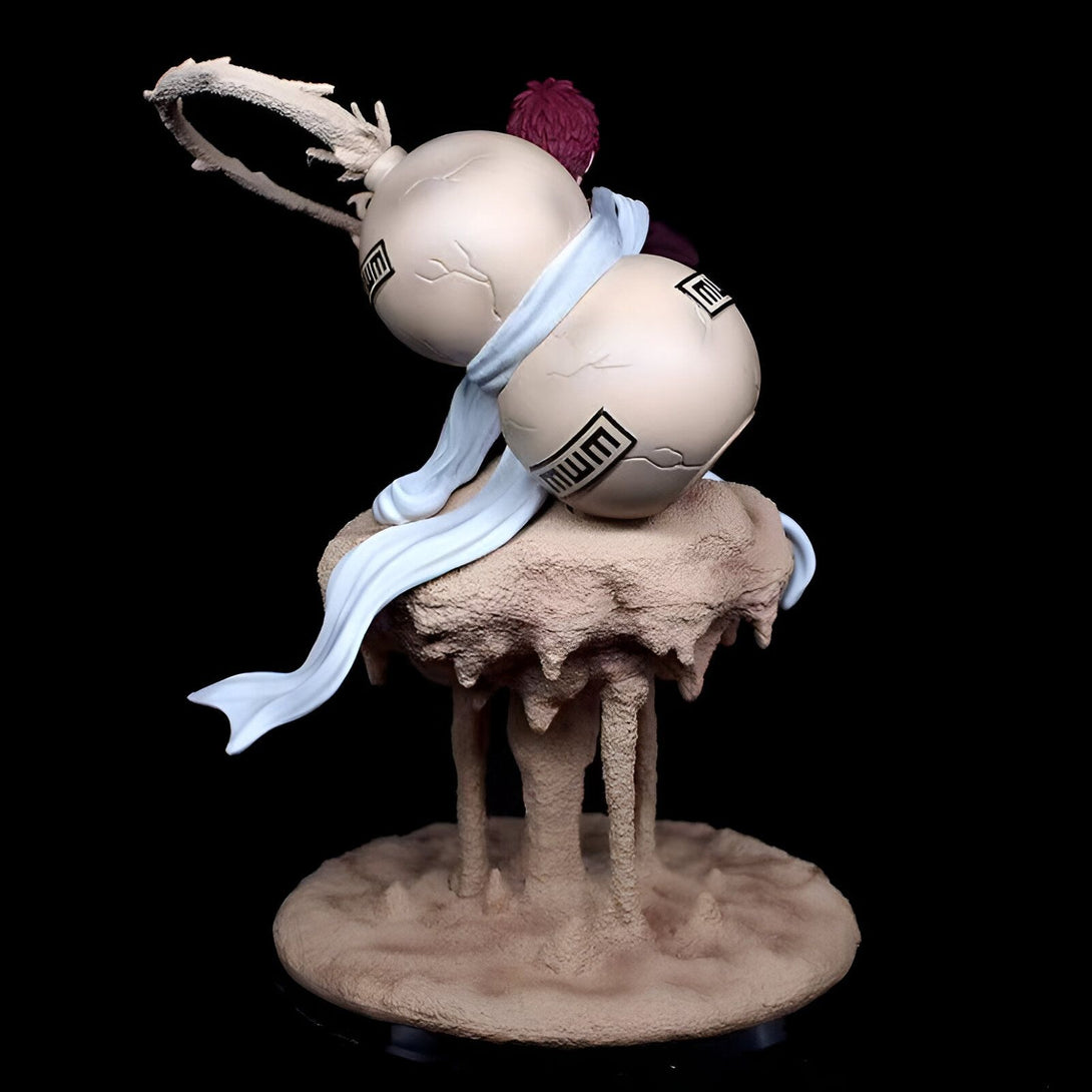 Statue de Deidara, un personnage de l'anime Naruto, tenant ses bombes et debout sur un socle de sable. La statue est représentée dans sa posture de combat, ses bombes étant prêtes à exploser.