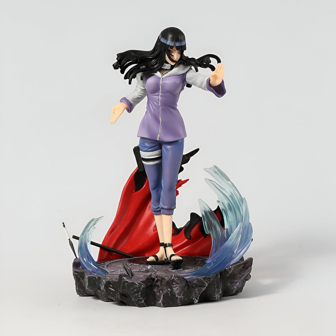 Hinata Hyuga, personnage de l'anime Naruto, en figurine posable, vêtue d'une tenue violette et d'une cape rouge. Elle est représentée avec ses cheveux noirs et ses yeux violets. La figurine est posée sur un socle noir et bleu, avec des effets de mouvement de chakra.