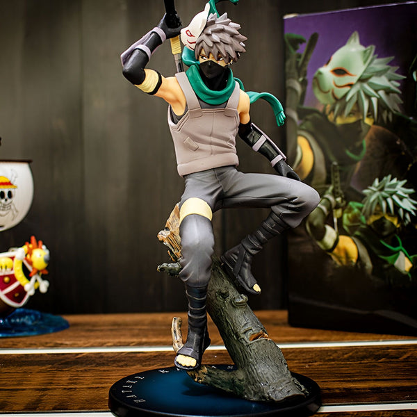 Figurine de Kakashi Hatake de Naruto Shippuden, portant son masque et sa tenue classique, assis sur un tronc d'arbre. La figurine est posée sur une base noire et est accompagnée de son emballage original.