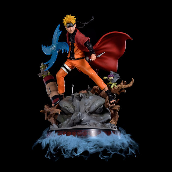 Statue de Naruto Uzumaki dans une pose dynamique, tenant un Rasengan bleu et portant son manteau rouge emblématique. Il est accompagné de ses deux invocations, Gamakichi et Gamabunta. La base de la statue est ornée d'une fumée bleue et représente un rocher.