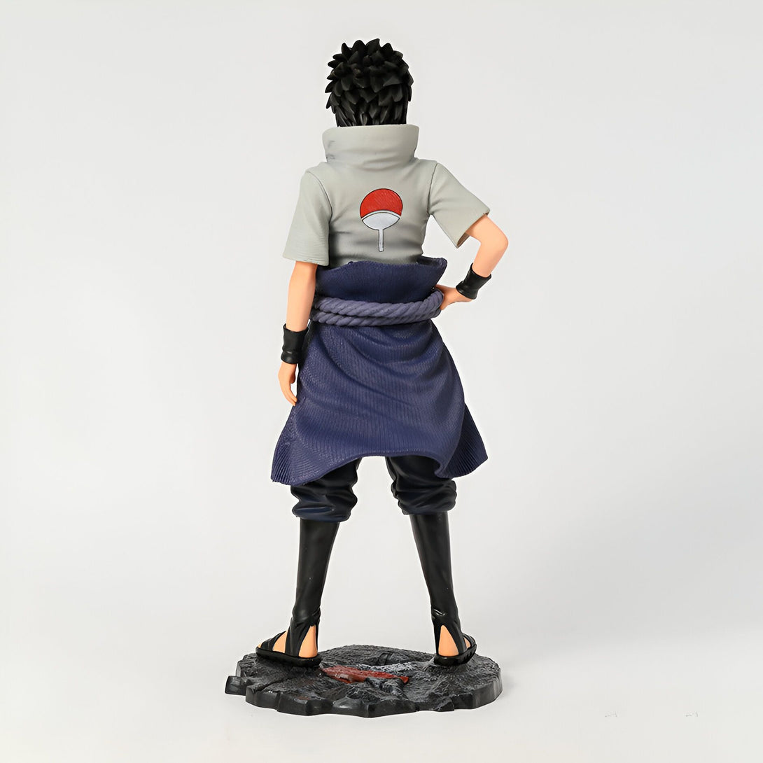 Figure de collection de Naruto Shippuden représentant Kakashi Hatake de dos, portant son emblématique costume blanc avec le symbole du Sharingan sur le dos.  Il porte également ses sandales et son pantalon noir ainsi qu'un long manteau bleu.  La figurine est debout sur une base noire et est prête à être exposée.