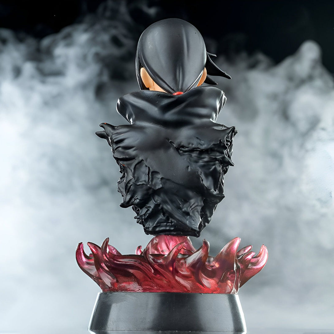 Statuette de Naruto Shippuden représentant Itachi Uchiha, portant son célèbre manteau noir et debout sur un socle de flammes rougeoyantes.  Le fond est flou et légèrement brumeux, créant une atmosphère mystique.