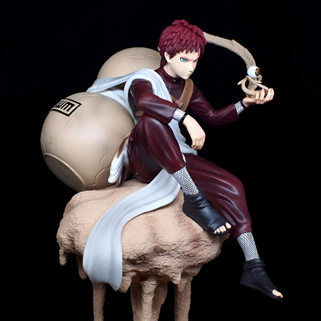 Figurine de Pain, personnage de l'anime Naruto, assis sur une base de sable, tenant un œil dans sa main et portant des gourdins sur son dos.