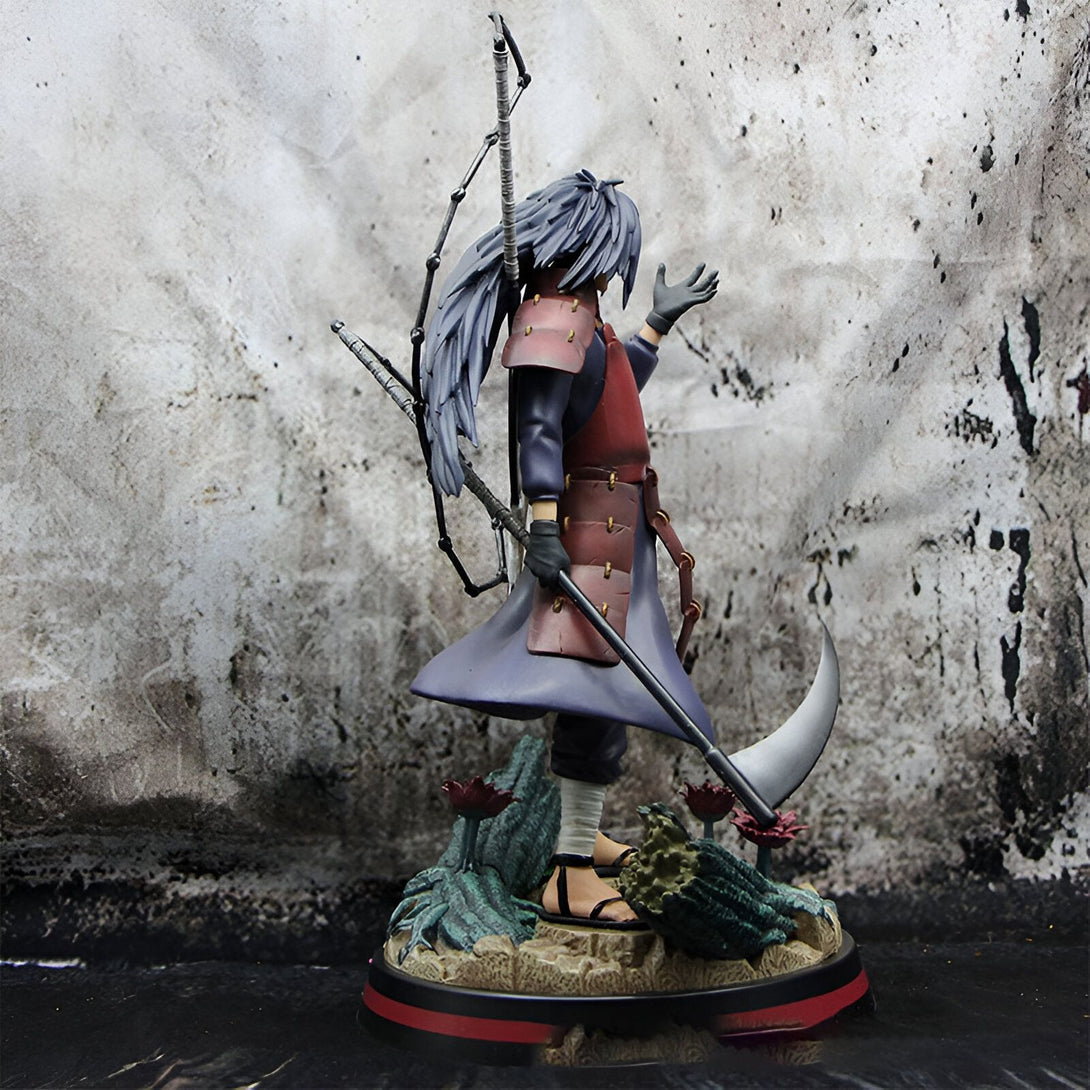 Statue de Pain, un personnage du manga Naruto, tenant une arme à longue portée et debout sur une base décorée de plantes et de sable.