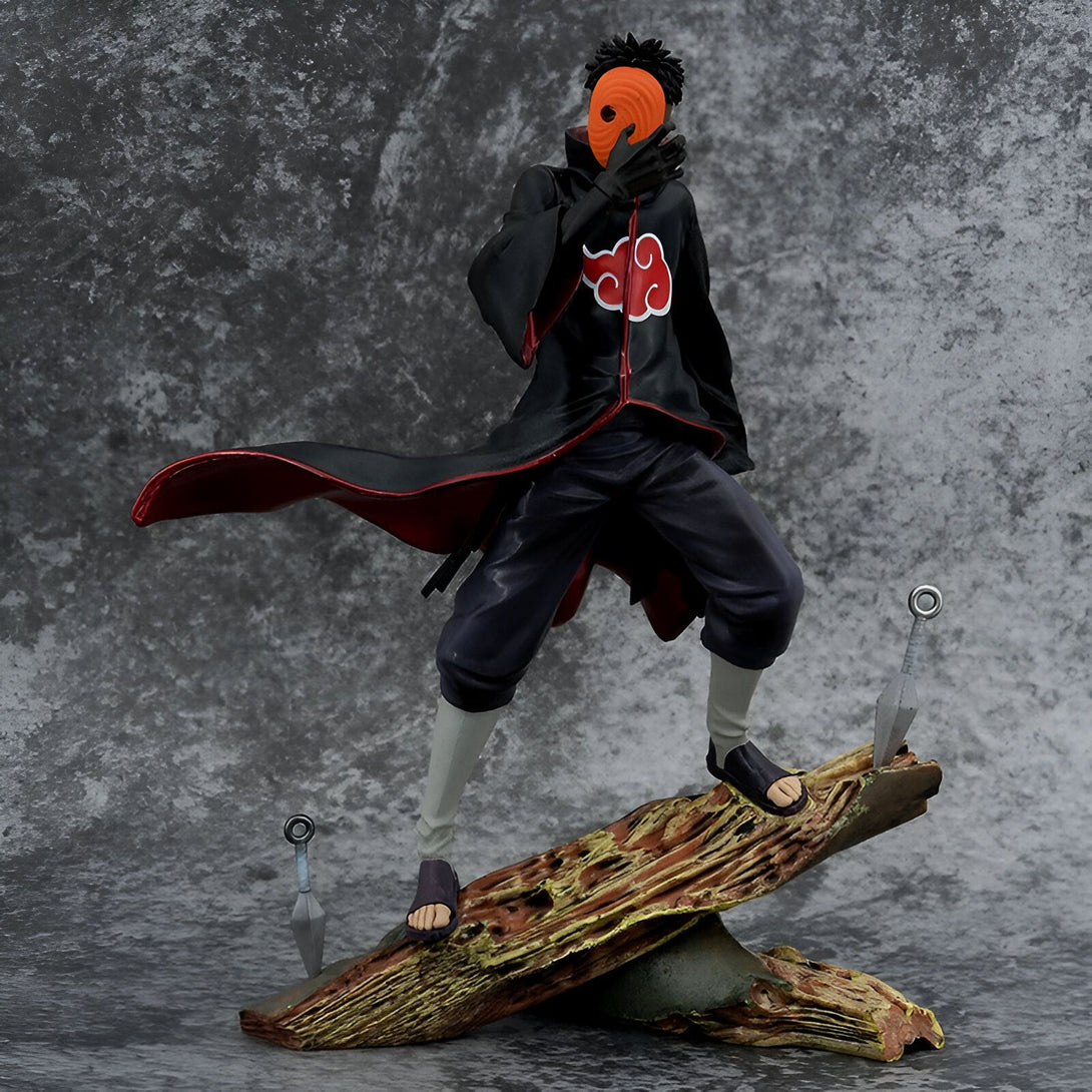 Figurine de Obito Uchiha, un personnage de l'anime Naruto, portant un masque orange et une cape rouge avec le symbole de l'Akatsuki, debout sur un morceau de bois.