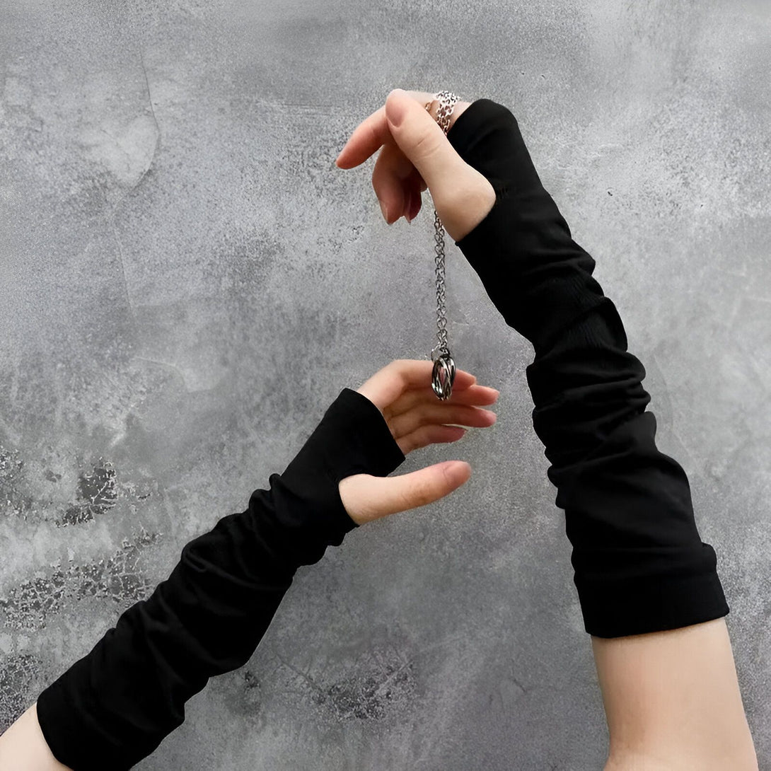 Une paire de mitaines noires en coton, portées sur les deux mains, tenant un collier en argent avec un pendentif rond. Les mitaines sont en tissu extensible et confortables, parfaites pour l'automne et l'hiver. Elles sont également très élégantes et s'accordent parfaitement avec une tenue décontractée. Le collier est en argent massif et est décoré d'un pendentif rond. Il est parfait pour compléter votre look et ajouter une touche de style à votre tenue.