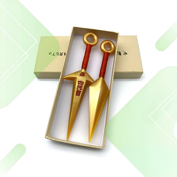 Deux kunaï dorés, armes de lancer utilisées par les ninjas dans l'univers de Naruto, dans leur boîte d'origine.  Les kunaï sont ornés du symbole du village caché de Konoha.