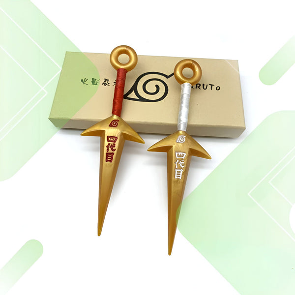 Deux kunais dorés de Naruto avec le symbole du village de Konoha et l'inscription "Sharingan" en kanji rouge et blanc. Les kunais sont posés sur une boîte en carton.
