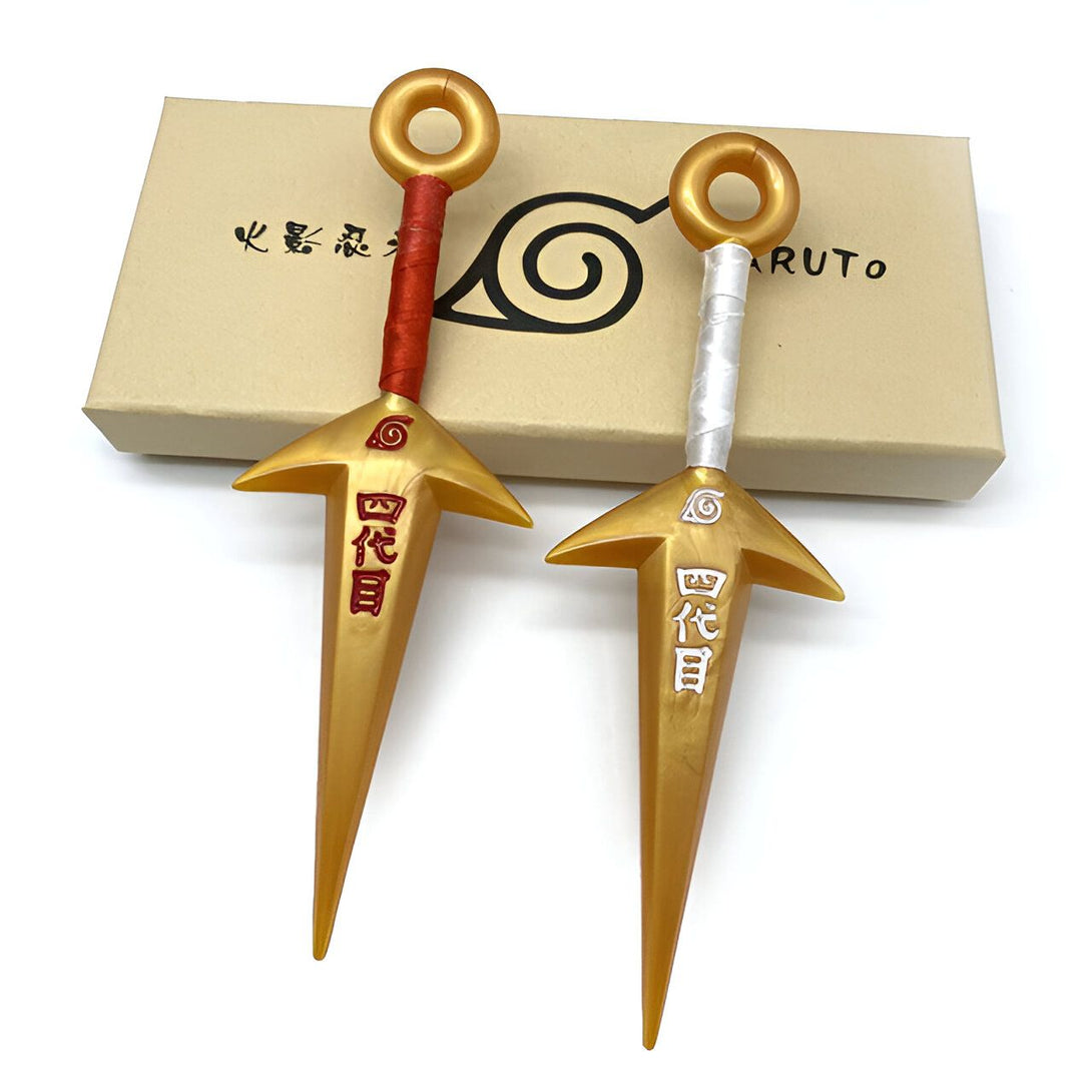 Deux kunais dorées de Naruto avec des cordes rouges et blanches. Les kunais ont l'inscription "Sharingan" en kanji sur la lame. Les kunais sont posés sur une boîte en carton avec l'emblème de Konoha.