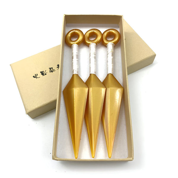 Trois kunais dorées, des armes de jet traditionnelles japonaises, dans un coffret en bois. Ces kunais sont des objets de collection pour les fans de Naruto.