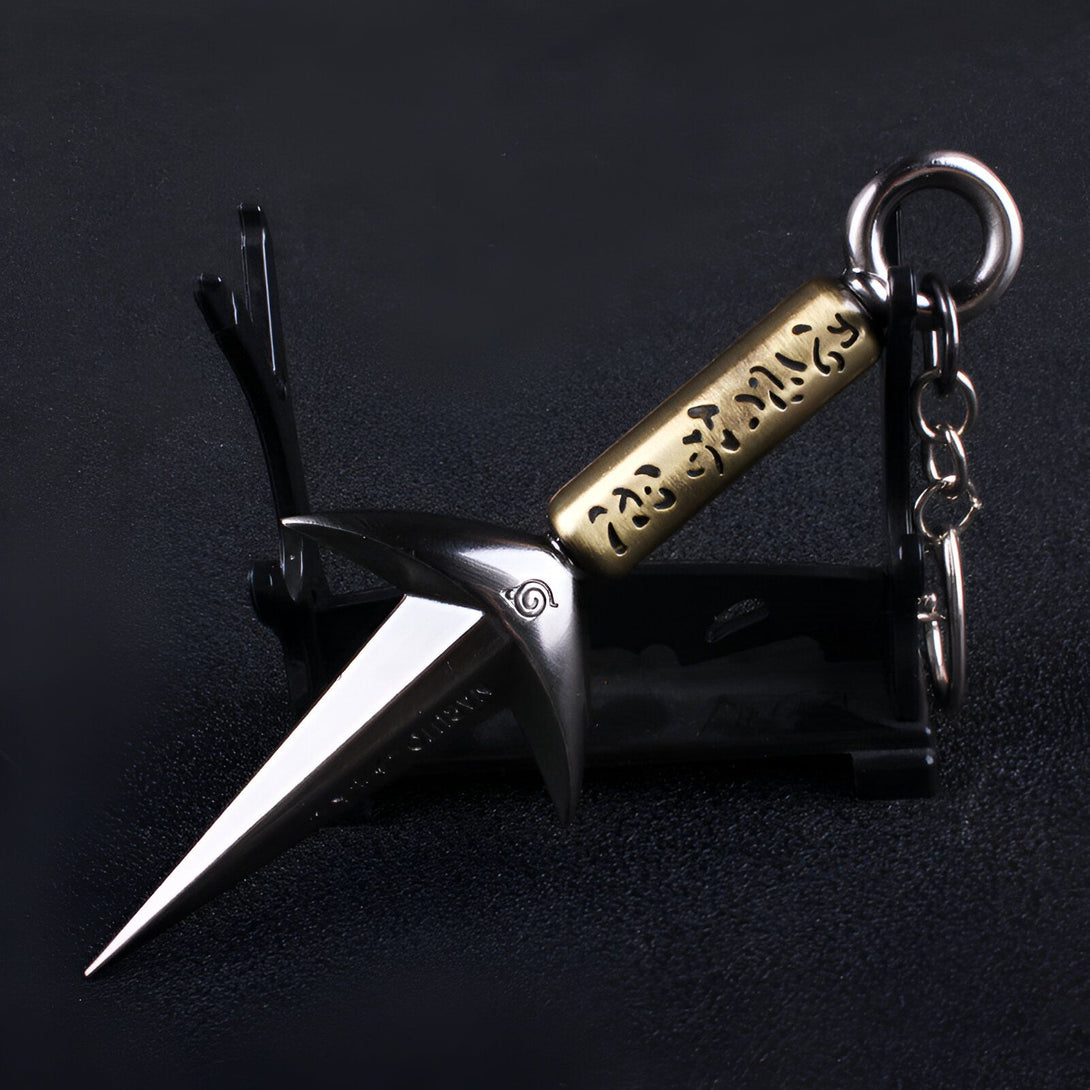 Porte-clés en forme de kunai, arme traditionnelle japonaise, orné du symbole du clan Uchiwa et de l'inscription "Sharingan" en japonais.