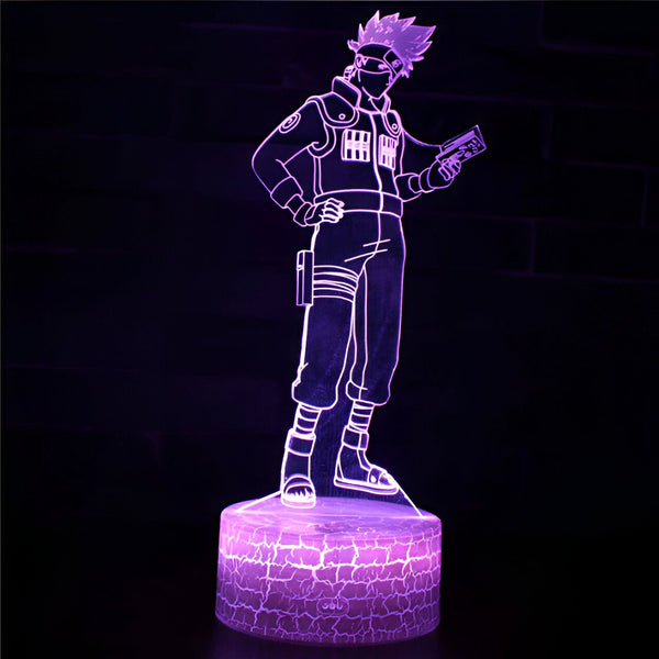 Lampe de nuit 3D représentant Kakashi Hatake, un personnage de l'anime Naruto, tenant un livre et portant son masque. La lampe est sur une base en forme de pierre.