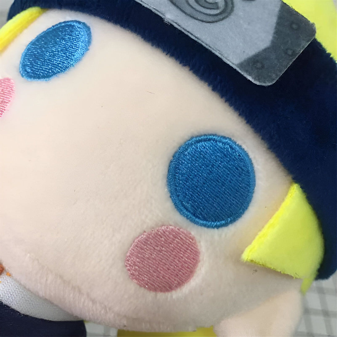 Peluche Naruto avec des yeux bleus et une joue rose, portant un bandeau de ninja.