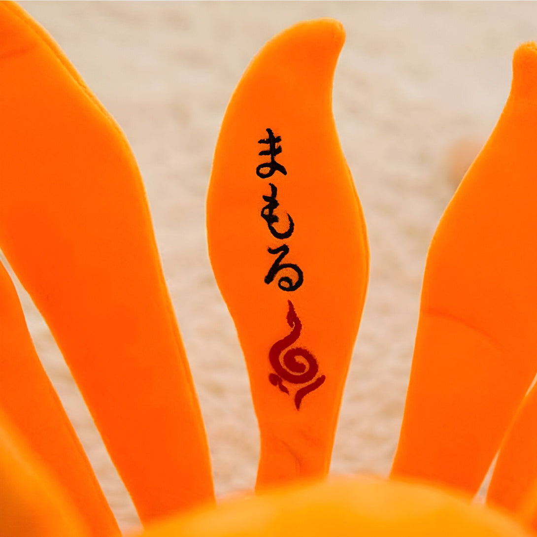 Une peluche orange en forme de queue de renard à neuf queues, avec le symbole de Naruto et l'inscription "Naruto" en japonais.