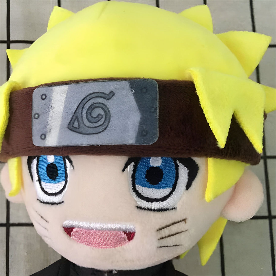 Peluche Naruto Uzumaki avec un bandeau frontal arborant le symbole du village de Konoha. Il est représenté avec ses yeux bleus et ses cheveux blonds.