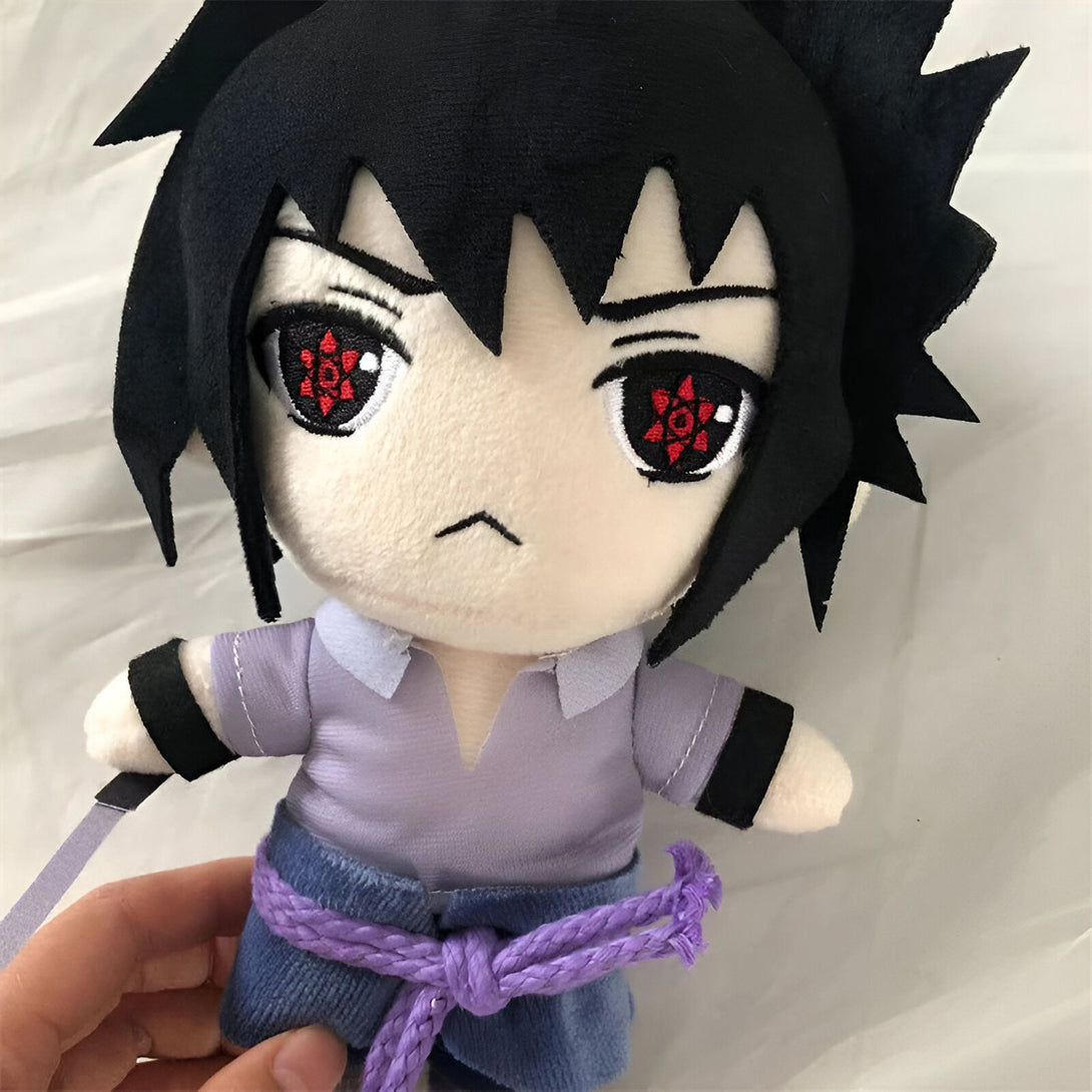 Peluche de Sasuke Uchiha, un personnage du manga et anime Naruto, portant sa tenue violette et son bandeau frontal avec le symbole du clan Uchiha.