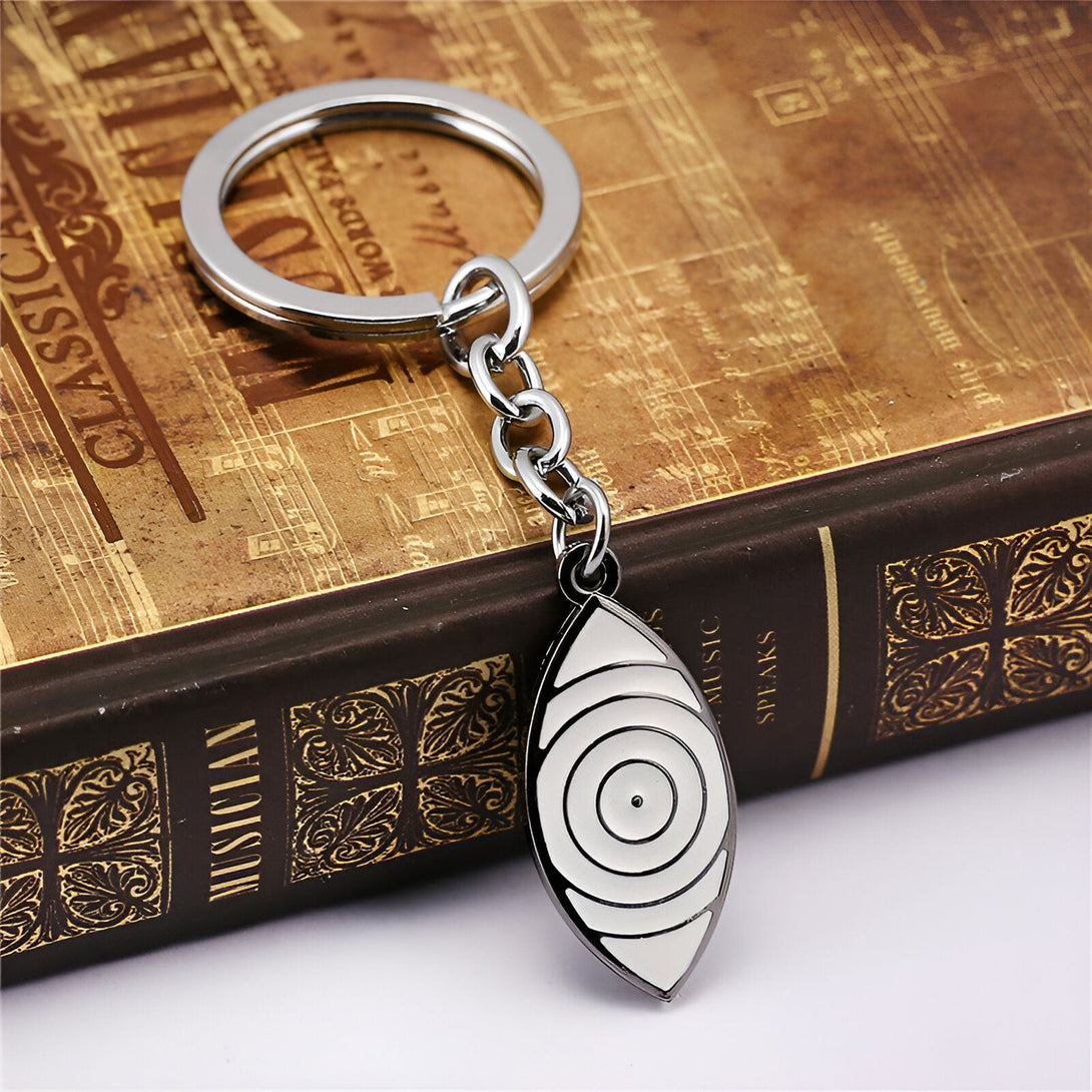 Porte-clés en métal argenté avec un pendentif en forme d'œil blanc sur un fond de livre ancien.