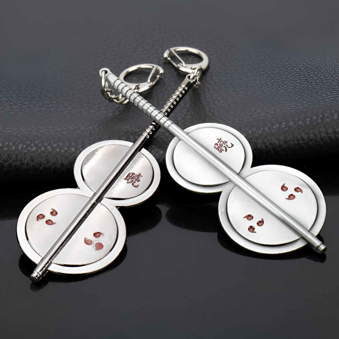 Porte-clés Naruto avec deux disques métalliques ornés de trois clous rouges, reliés par une barre métallique. Les disques affichent l'inscription "Sharingan" en kanji.