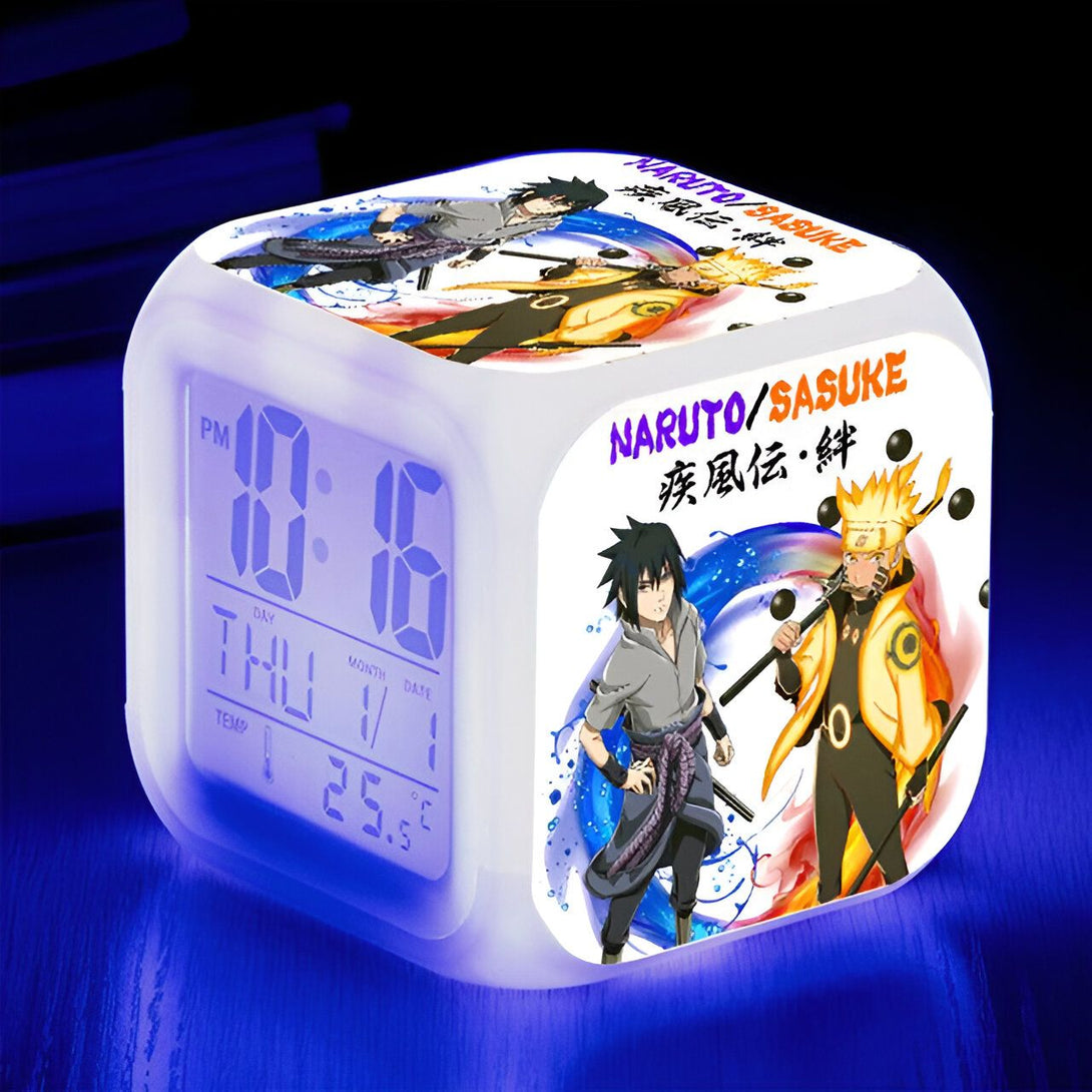 Horloge numérique blanche avec des personnages de l'anime Naruto et Sasuke. L'horloge affiche l'heure, le jour, le mois et la température.  L'horloge est éclairée d'une lumière bleue.