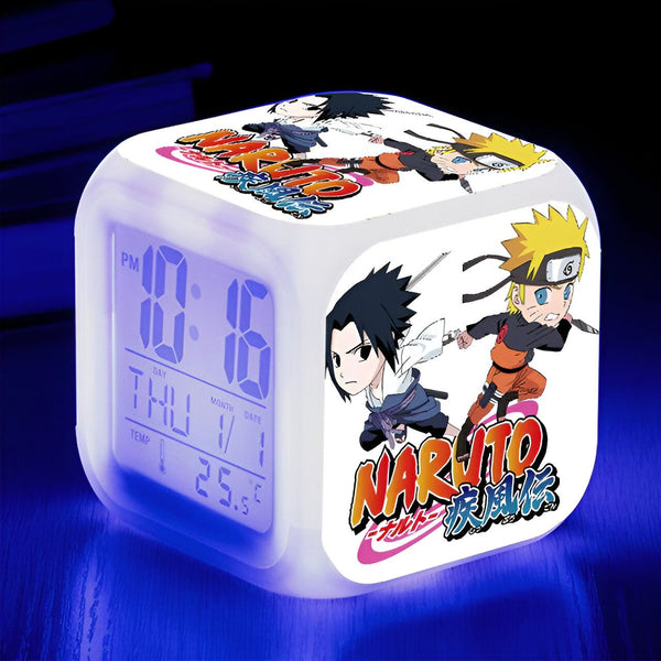 Réveil numérique blanc avec un design Naruto, mettant en scène Sasuke et Naruto. L'horloge affiche l'heure, le jour de la semaine, la température et la date. L'horloge est éclairée par une lumière bleue.