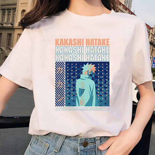 Un t-shirt blanc avec l'impression d'un personnage de manga Naruto, Kakashi Hatake, portant un uniforme bleu et blanc. Le personnage est représenté de dos avec un motif floral bleu et blanc. Le nom du personnage est imprimé trois fois en lettres orange sur le t-shirt.