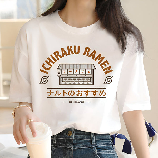 Une femme porte un t-shirt blanc avec un dessin de restaurant de ramen Ichiraku, le restaurant préféré de Naruto. Le t-shirt a le logo du village de Konoha et le texte "Naruto's favorite" en japonais.
