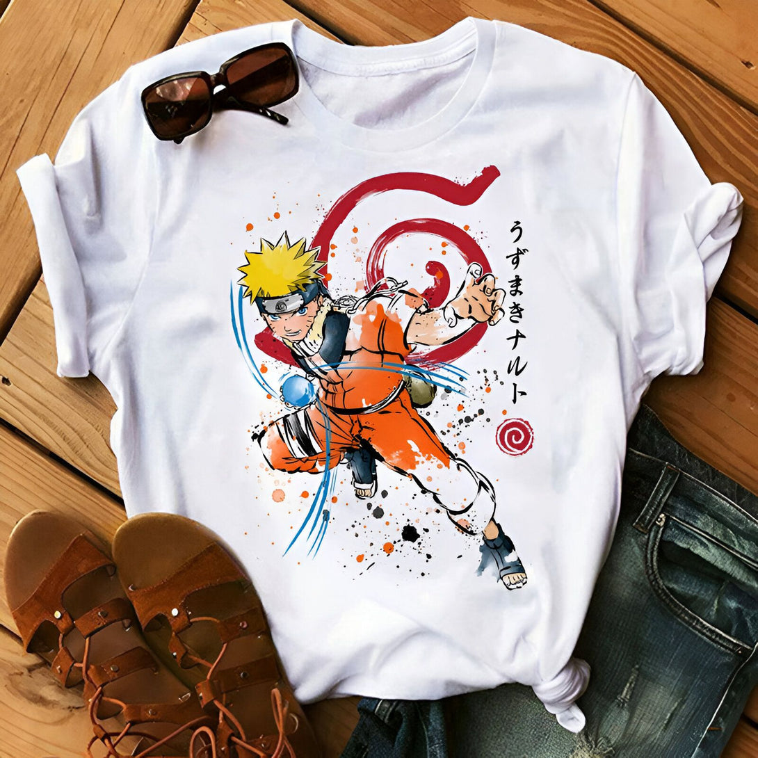 T-shirt blanc avec un imprimé de Naruto Uzumaki en action, portant sa tenue orange emblématique et effectuant le Rasengan. Le logo de Konoha est également présent, ainsi que des éclaboussures de peinture. Le t-shirt est posé sur un fond en bois et accompagné d'une paire de sandales.
