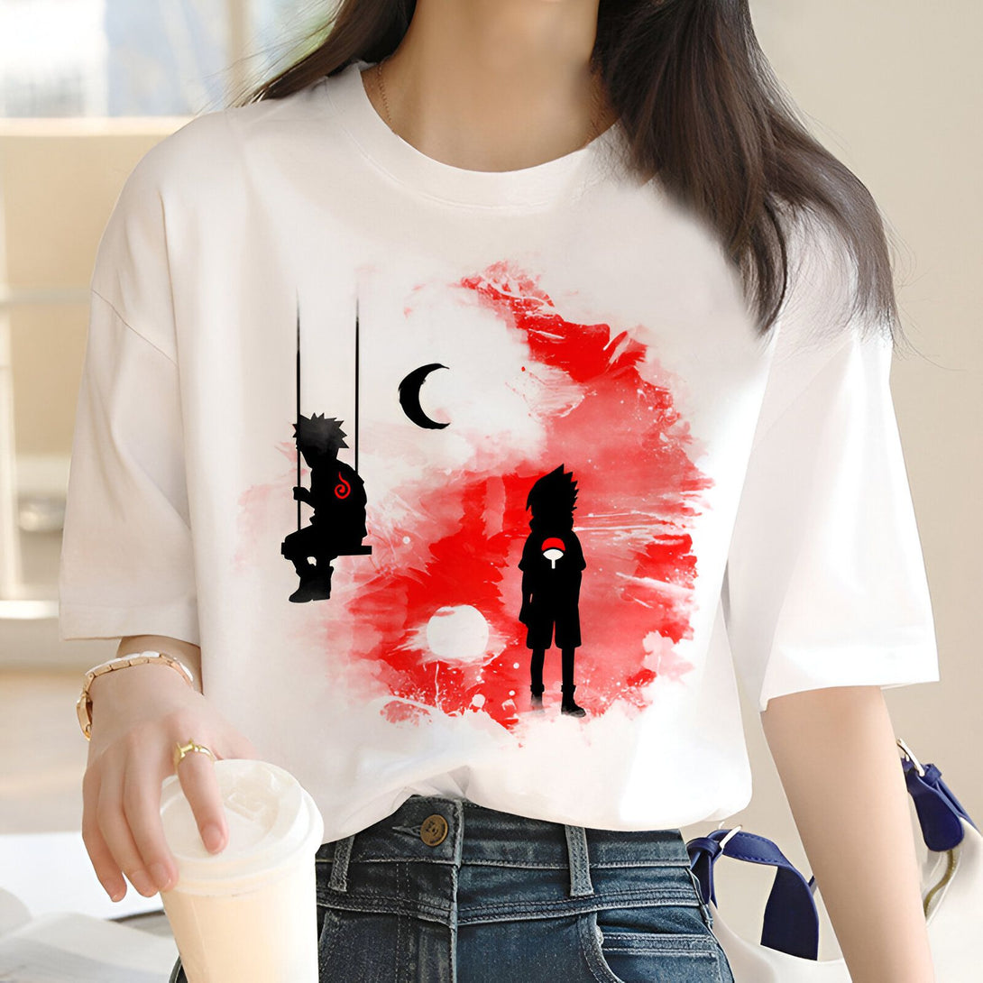 Une femme porte un t-shirt blanc avec un imprimé de Naruto et Sasuke. Naruto est sur une balançoire et Sasuke se tient debout. Le fond est rouge avec des éclaboussures de peinture et une lune.
