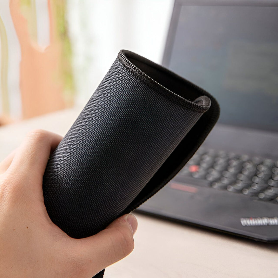 Un tapis de souris noir avec une texture en forme de zigzags, tenu dans une main devant un ordinateur portable.