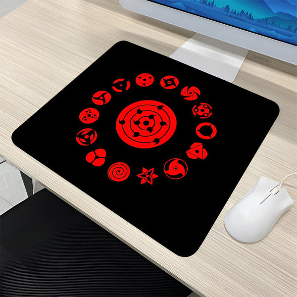 Un tapis de souris noir avec le symbole du Rinnegan et les emblèmes des différents Dojutsu de Naruto en rouge.  Le tapis est sur un bureau en bois.